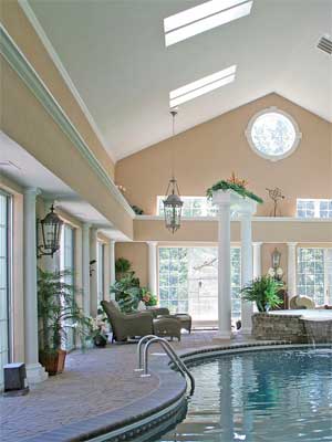 Luxurious indoor pool room with high ceilings, skylights, and lots of glass surrounding the pool deck
